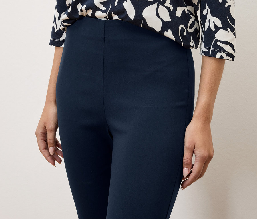 Közeli kép egy nőről, aki sötétkék nadrágot és virágmintás felsőt visel.