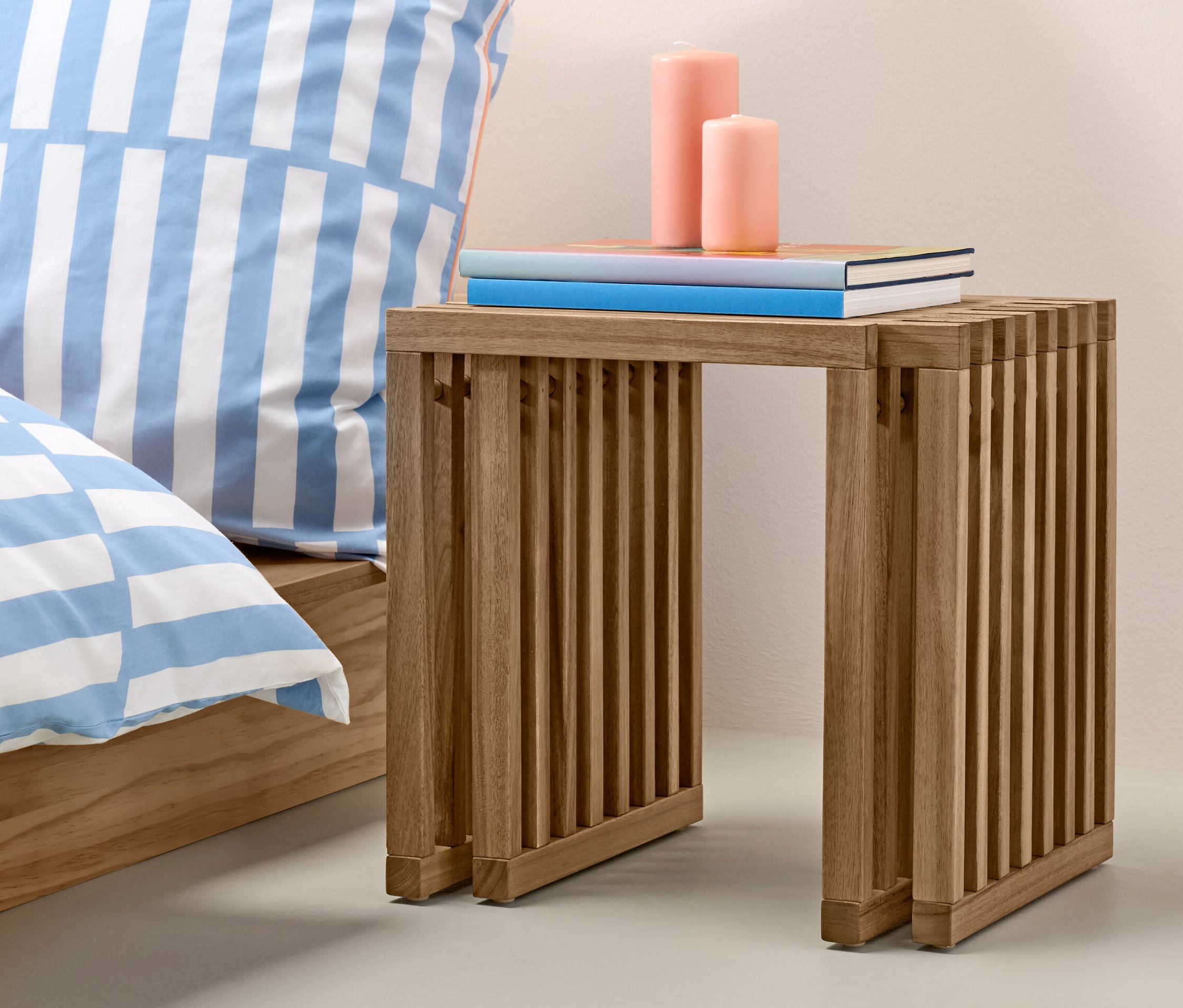 Kihúzható ülőke könyvekkel és gyertyákkal az ágy mellett és egy narancssárga váza.