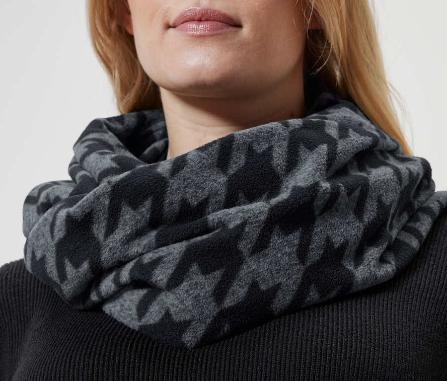 Egy szőke nő részlete szürke, kakasmintás sállal a nyakában és fekete pulóverrel.