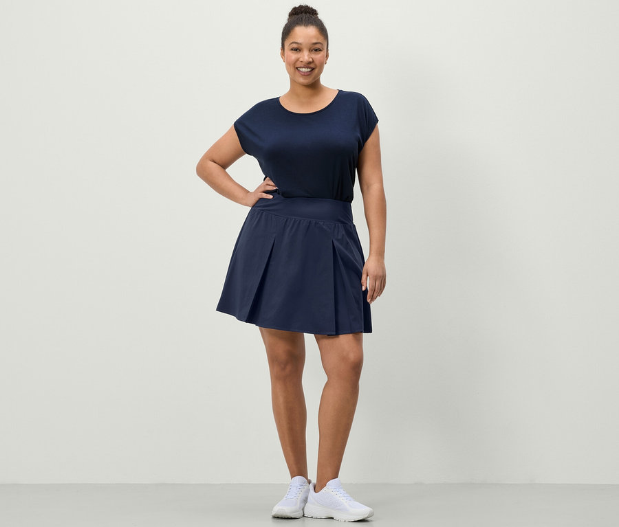 Nő pózol sötétkék sportszoknyában és kék sportfelsőben.