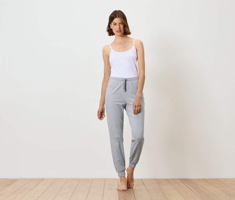 Nő áll fehér felsőben és szürke melegítőben, mezítláb.