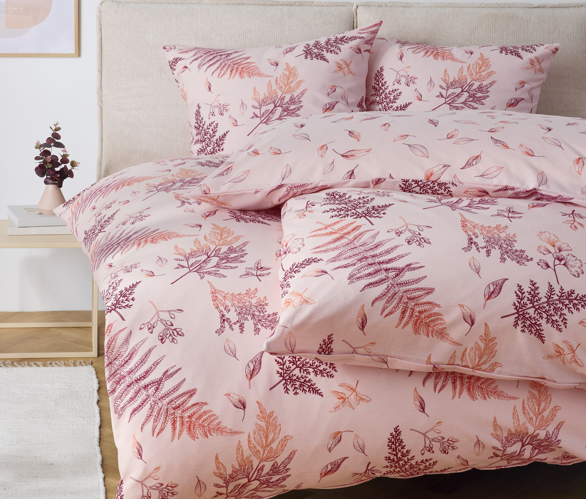 Rózsaszín ágynemű páfránymintával egy ágyon.