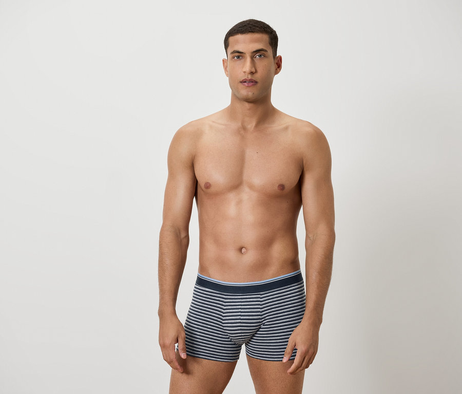 Férfi fedetlen felsőtesttel, kék-fehér csíkos alsónadrágban pózol.