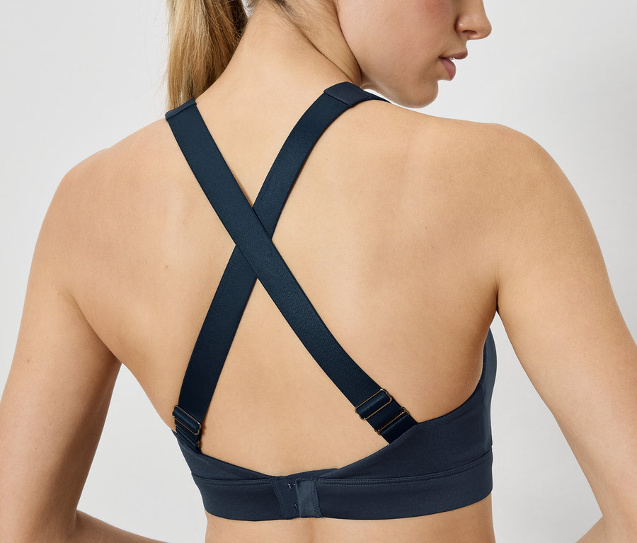 Hátulnézet egy nőről, aki sötétkék női sportmelltartót visel, melynek pántjai hátul keresztezettek.