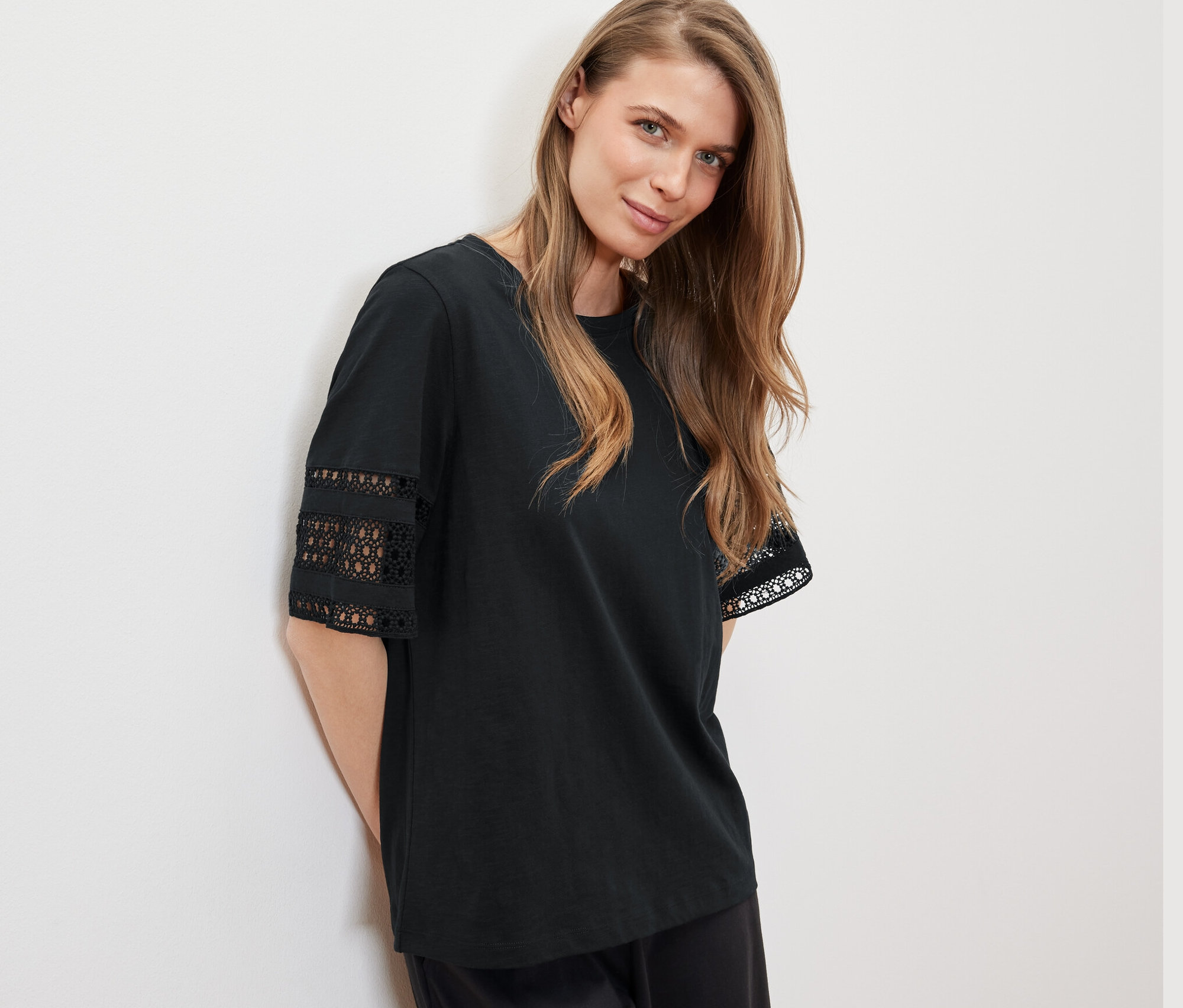 Egy nő a falnak dőlve fekete, hímzett női felsőt visel.