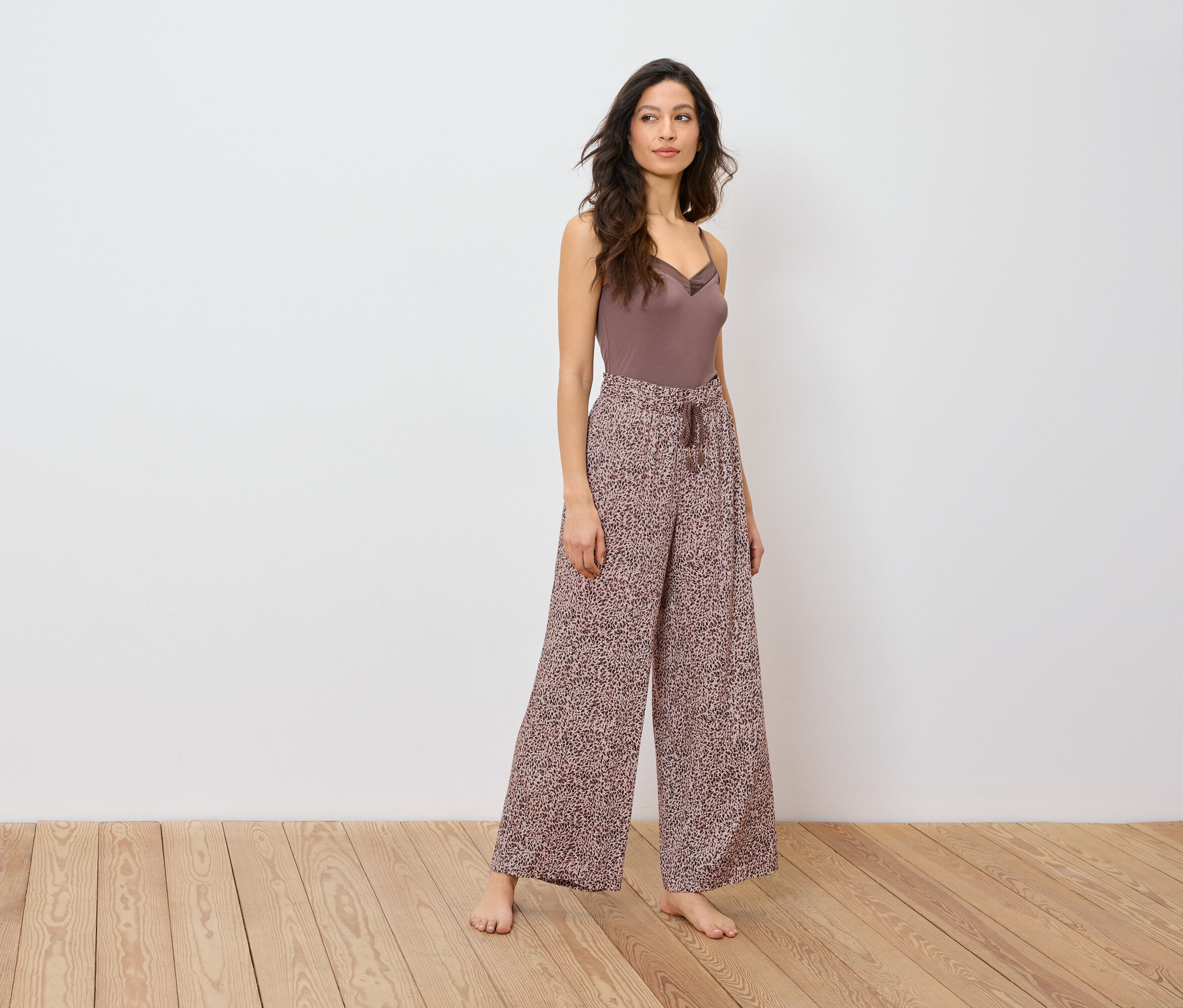 Nő pózol barna felsőben és bő, állatmintás nadrágban.