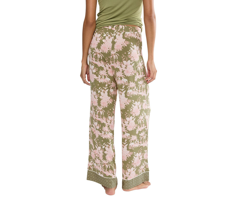 Hátulnézet egy zöld nadrágot viselő nőről rózsaszín virágmintával és zöld felsővel.