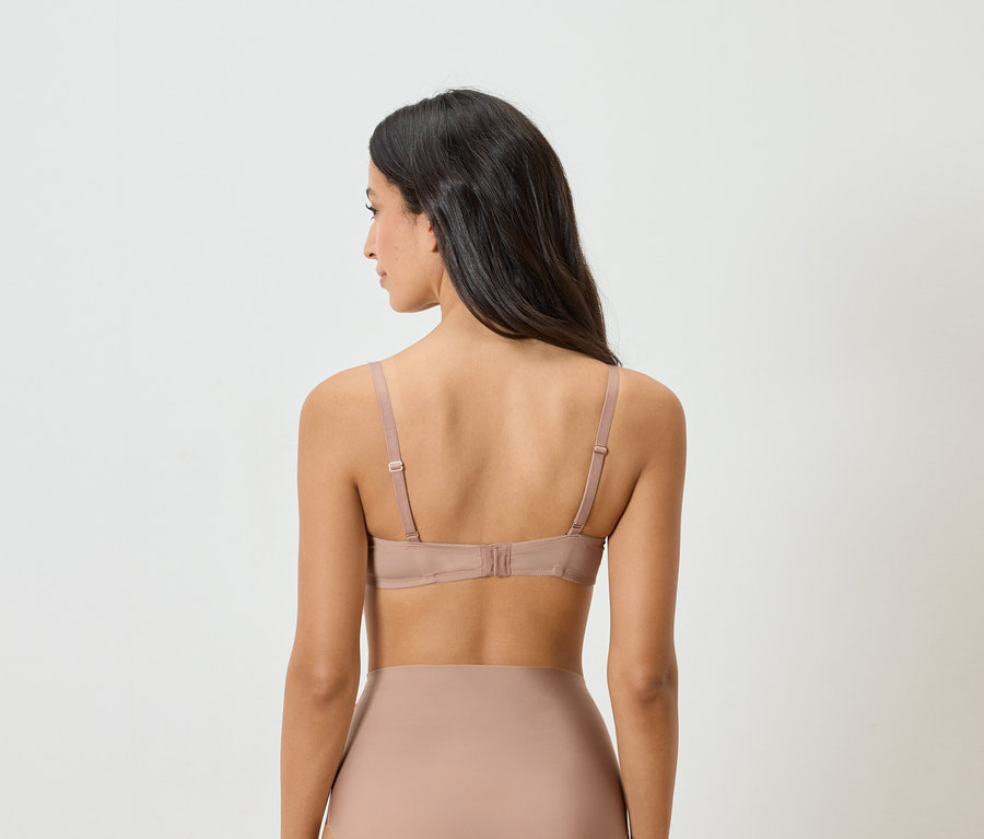 Hátulnézet egy sötét hajú nőről, aki testszínű melltartót és alsóneműt visel.