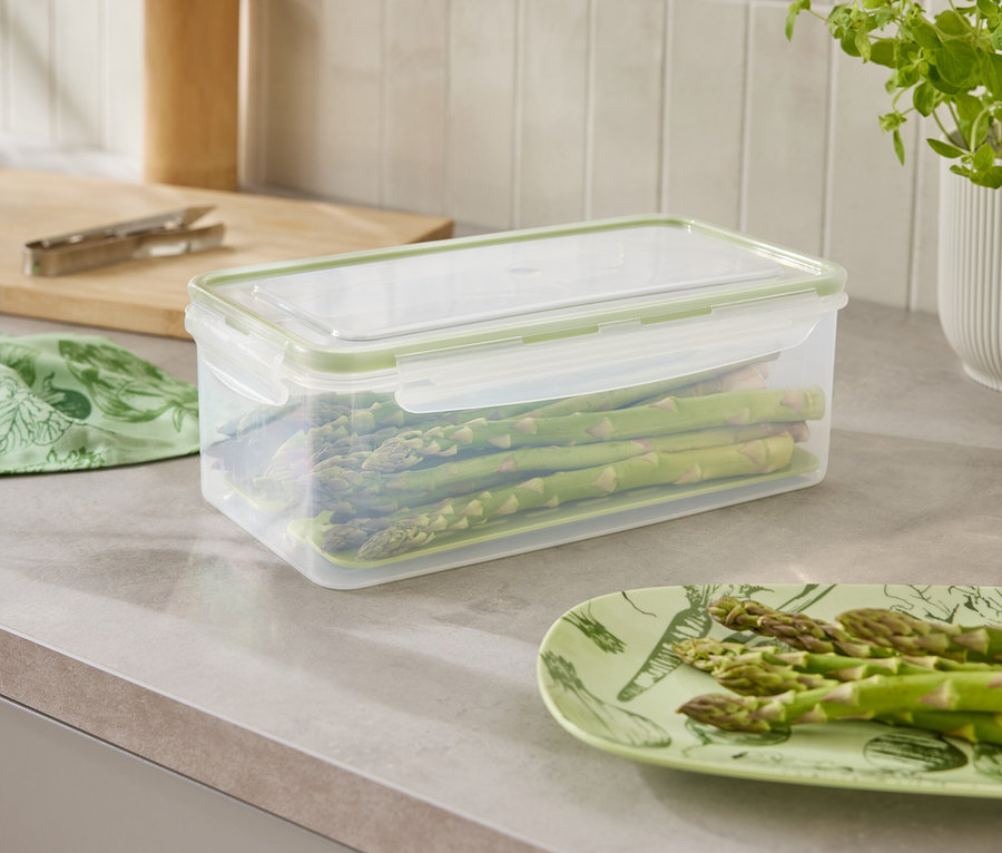 A konyhapulton egy spárgával teli tárolóedény, egy spárgával teli tányér és egy növény található.