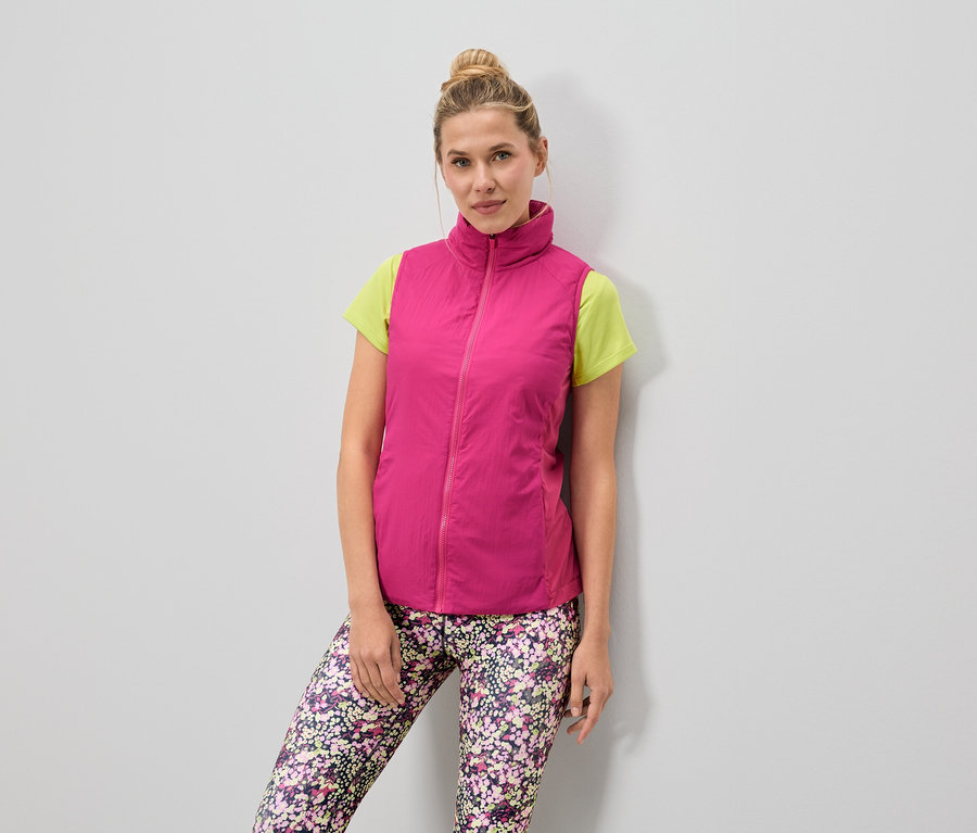Nő visel rózsaszín mellényt világoszöld póló felett és virágmintás leggingset.