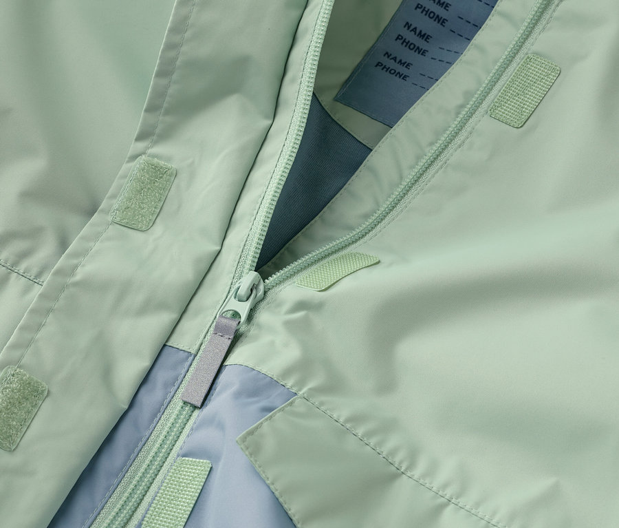 Egy kinyitott, mentazöld kabát közeli képe cipzárral és világoskék díszítéssel.