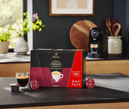 Fekete Cafissimo pure plus kávéfőző és egy csomag Espresso Intense - 96 db kávékapszula a pulton.