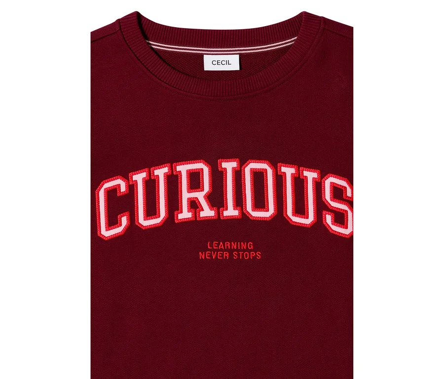 Bordó CECIL szabadidőfelső nagyméretű, piros-fehér hímzett „CURIOUS” felirattal és alatta „LEARNING NEVER STOPS” szöveggel.