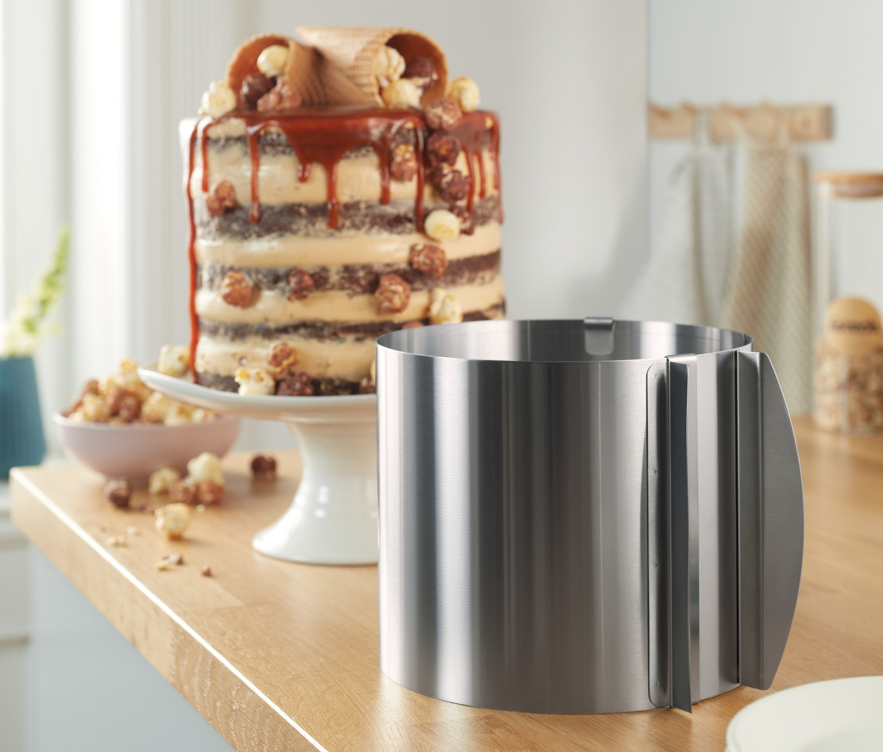 Egy nemesacél tortagyűrű áll a konyhapulton tányérok és egy torta mellett.