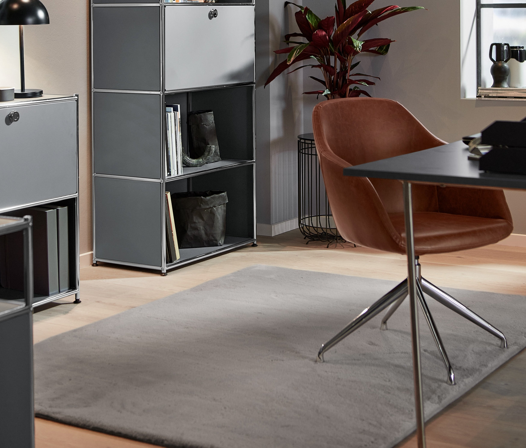 A szobában egy műbőr forgószék, egy magas fémpolc 1 ajtóval és egy LED-es asztali lámpa található. A földön egy hosszú szálú szőnyeg van.