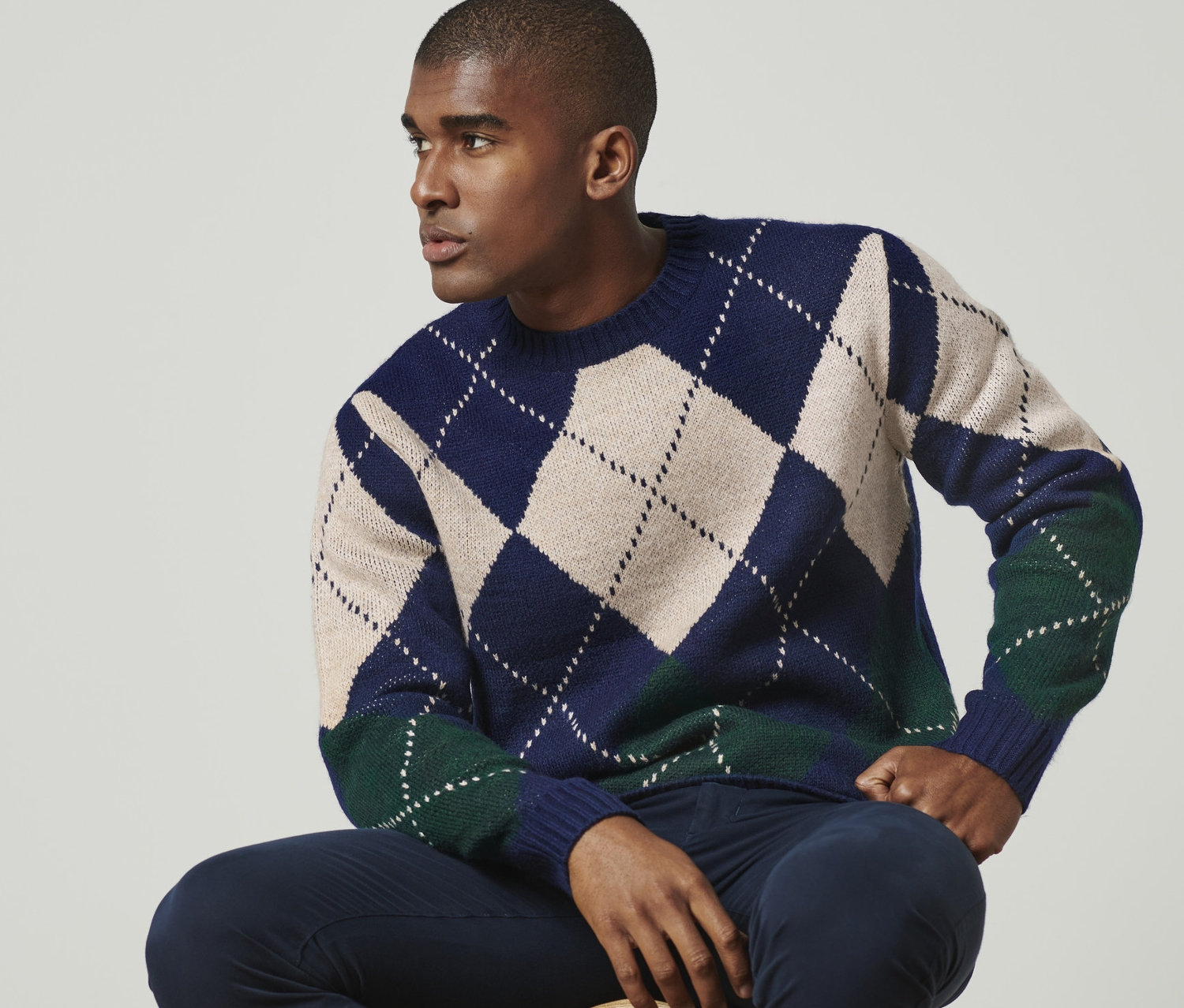 Férfi ül egy széken és sötétkék, kárómintás kötött pulóvert visel.