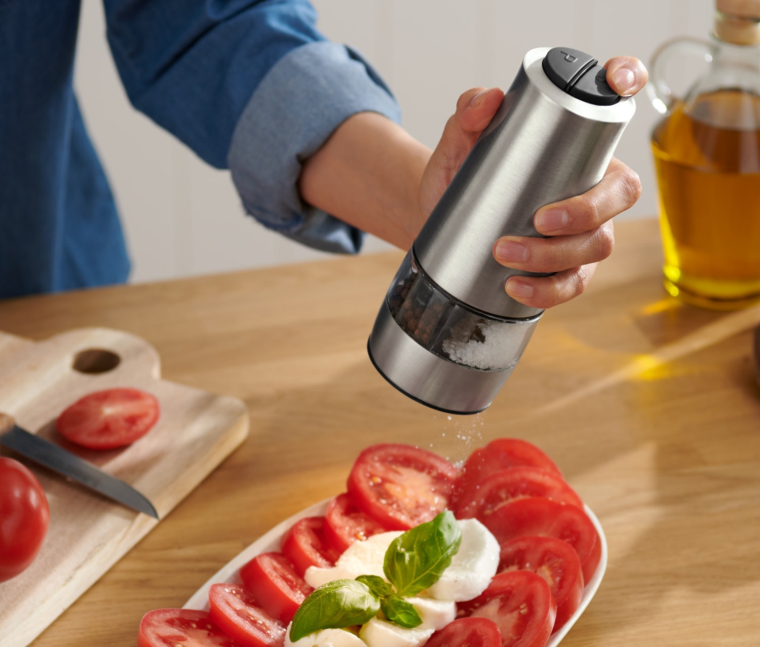 Nő fűszerezi a paradicsomot és a mozzarellát elektromos só- és borsőrlővel.