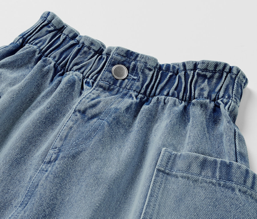 Egy világoskék lány farmerszoknya részlete gombos záródással és zsebekkel.