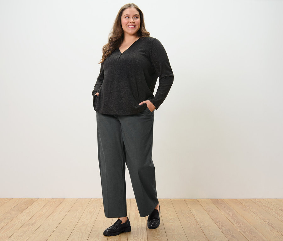 Nő kényelmes szövött nadrágban és csillogó blúzban pózol.