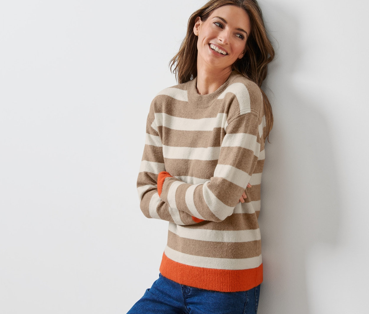 Egy nő mosolyogva dől a falnak egy csíkos kötött pulóverben.