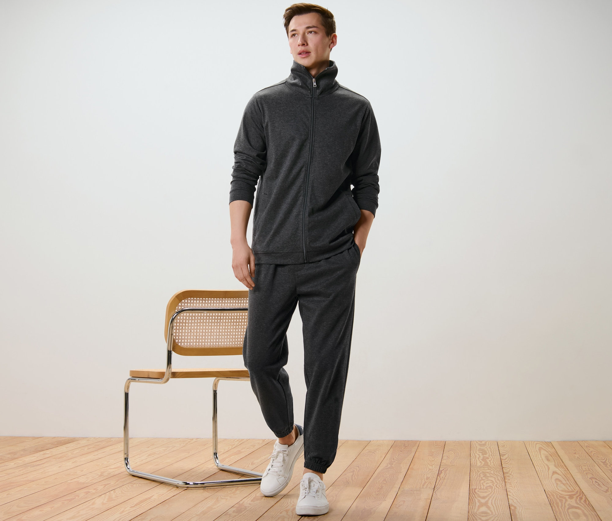 Férfi szabadidő szettben és fehér cipőben pózol egy szék mellett.