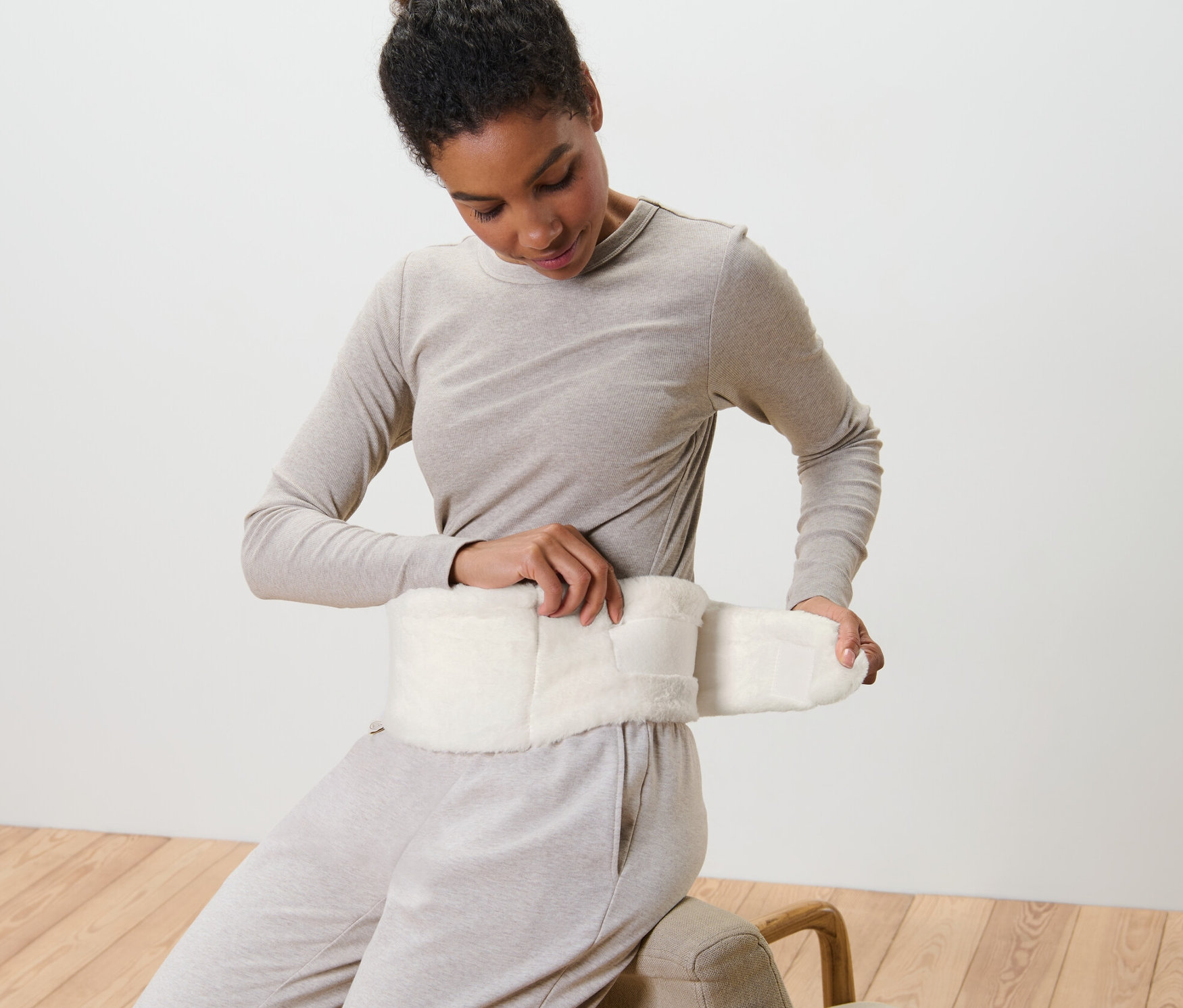 Nő rögzít egy melegvizes palackot plüss pánttal a dereka körül.