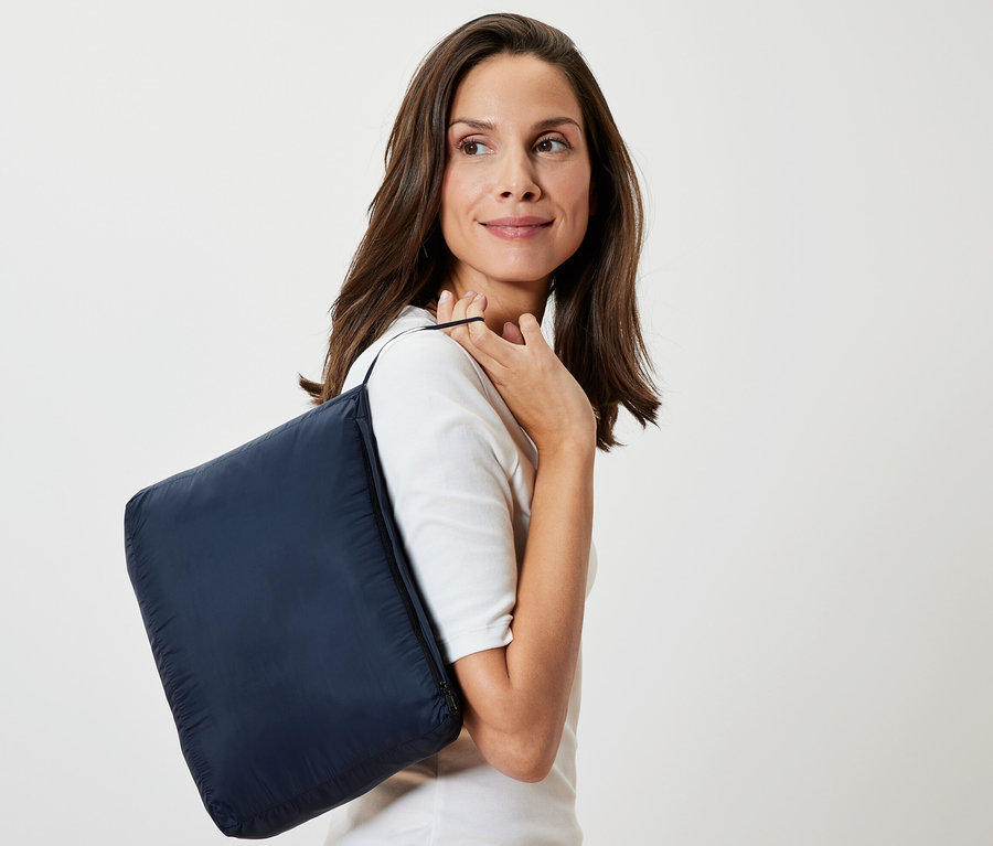 Nő sötétkék "Könnyű takaró utazáshoz" takaróval a vállán.