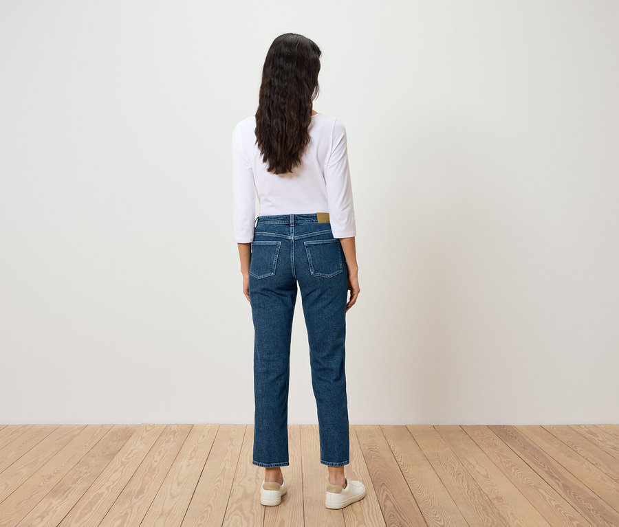 Hátulról látható egy hosszú, sötét hajú nő kék farmerban és fehér pólóban.