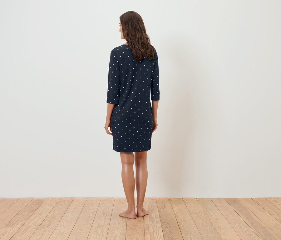 Egy nő háttal áll a kamerának, és sötétkék, fehér pöttyös ruhát visel.