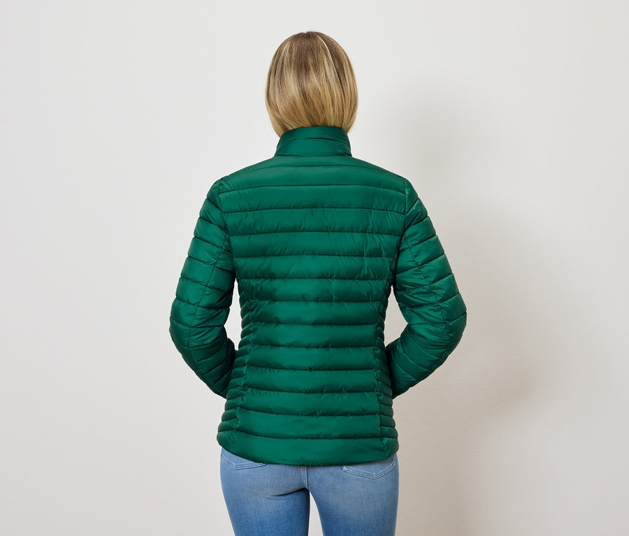 Hátulnézet egy szőke hajú nőről, aki zöld steppelt kabátot és kék farmert visel.