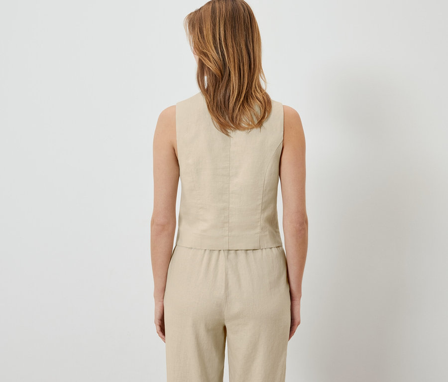 Hátulnézet egy nőről, aki vászonmellényt és nadrágot visel.