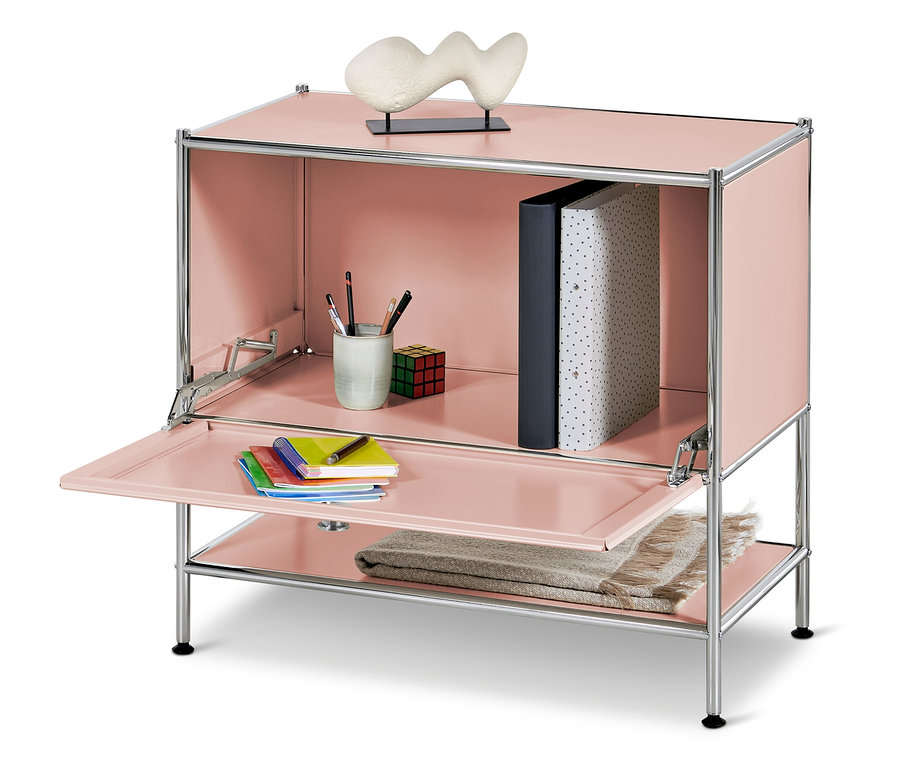 Rózsaszín szekrény nyitott ajtóval, belül pohár ceruzákkal, kocka és iratrendezők, az alsó polcon takaró, felül pedig egy szobor.