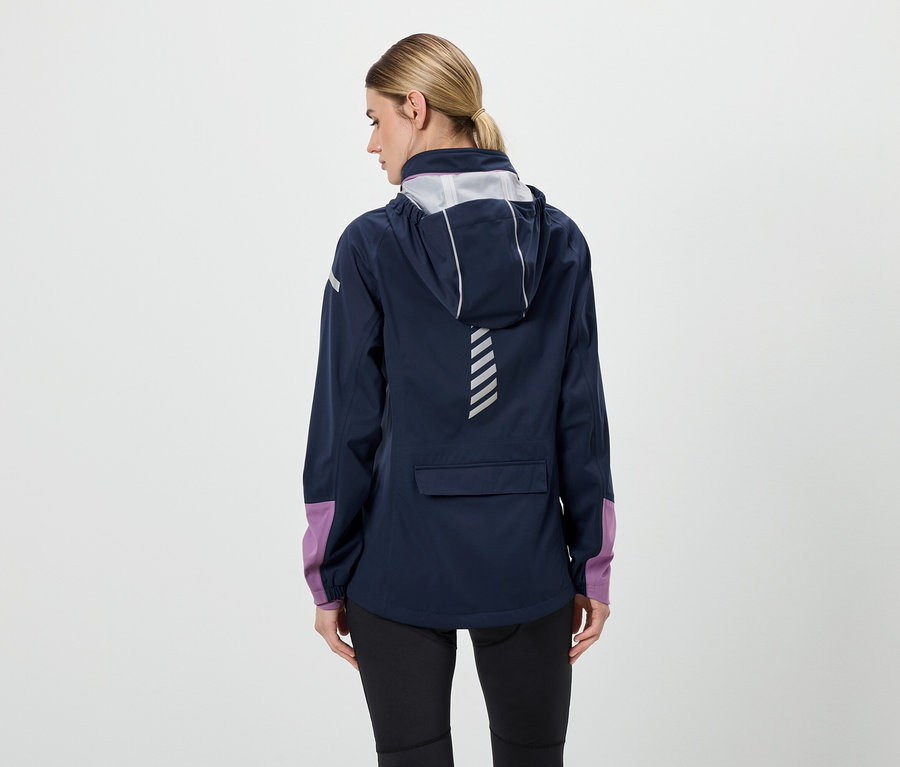 Hátulról látható egy nő sötétkék, kapucnis kabátban, fekete nadrágban és lila ujjakkal.