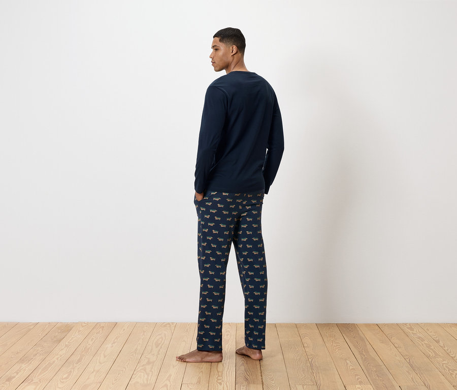 Hátulról látható férfi sötétkék tacskómintás pizsamában.
