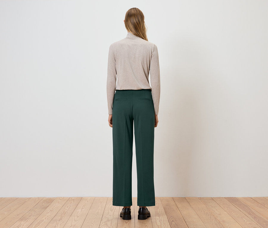 Hátulról látható nő bézs garbót és zöld nadrágot visel.