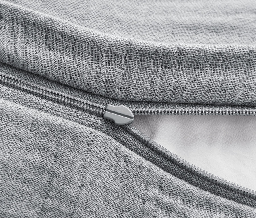 Egy szürke paplanhuzat részlete, cipzárral, ami részben nyitva van, és felfedi a fehér tölteléket.