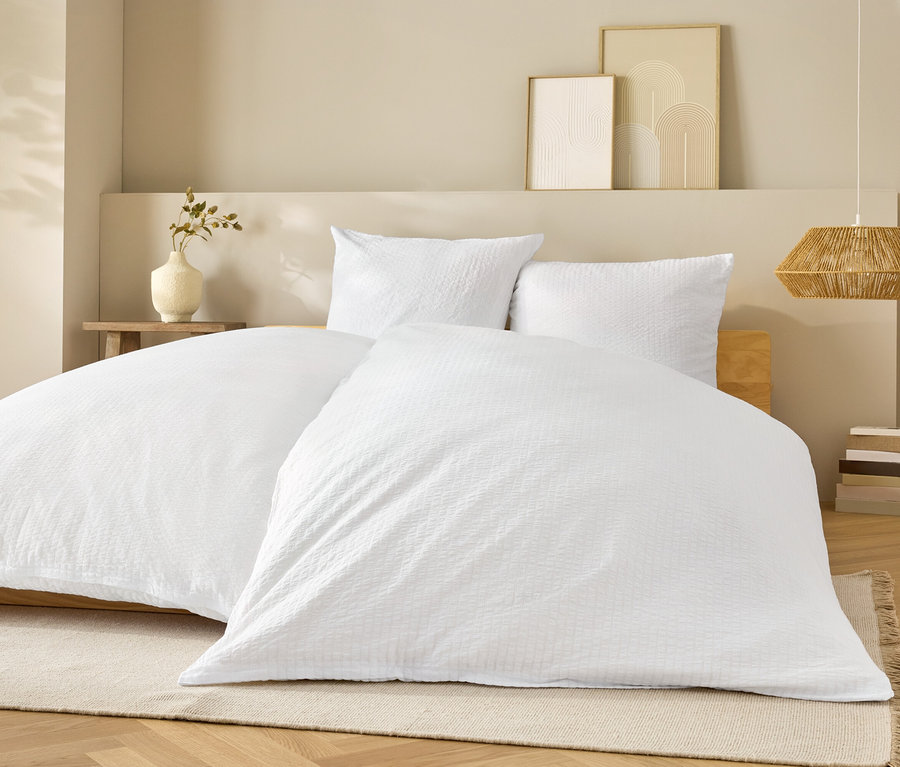 Fehér ágynemű fehér párnákkal egy ágyon.