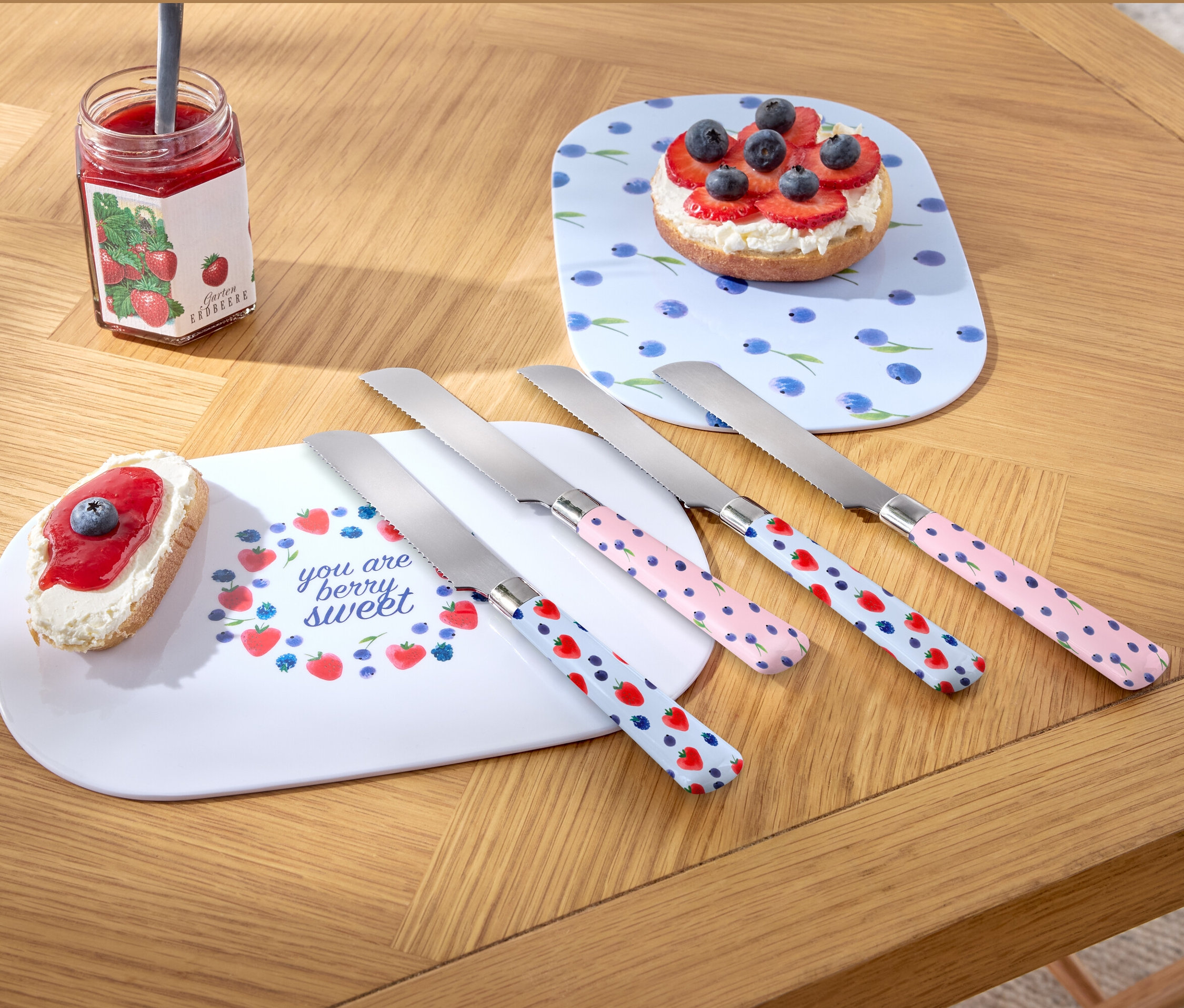 Négy reggelizőkés fekszik egy fa asztalon két tányér és egy üveg lekvár mellett.