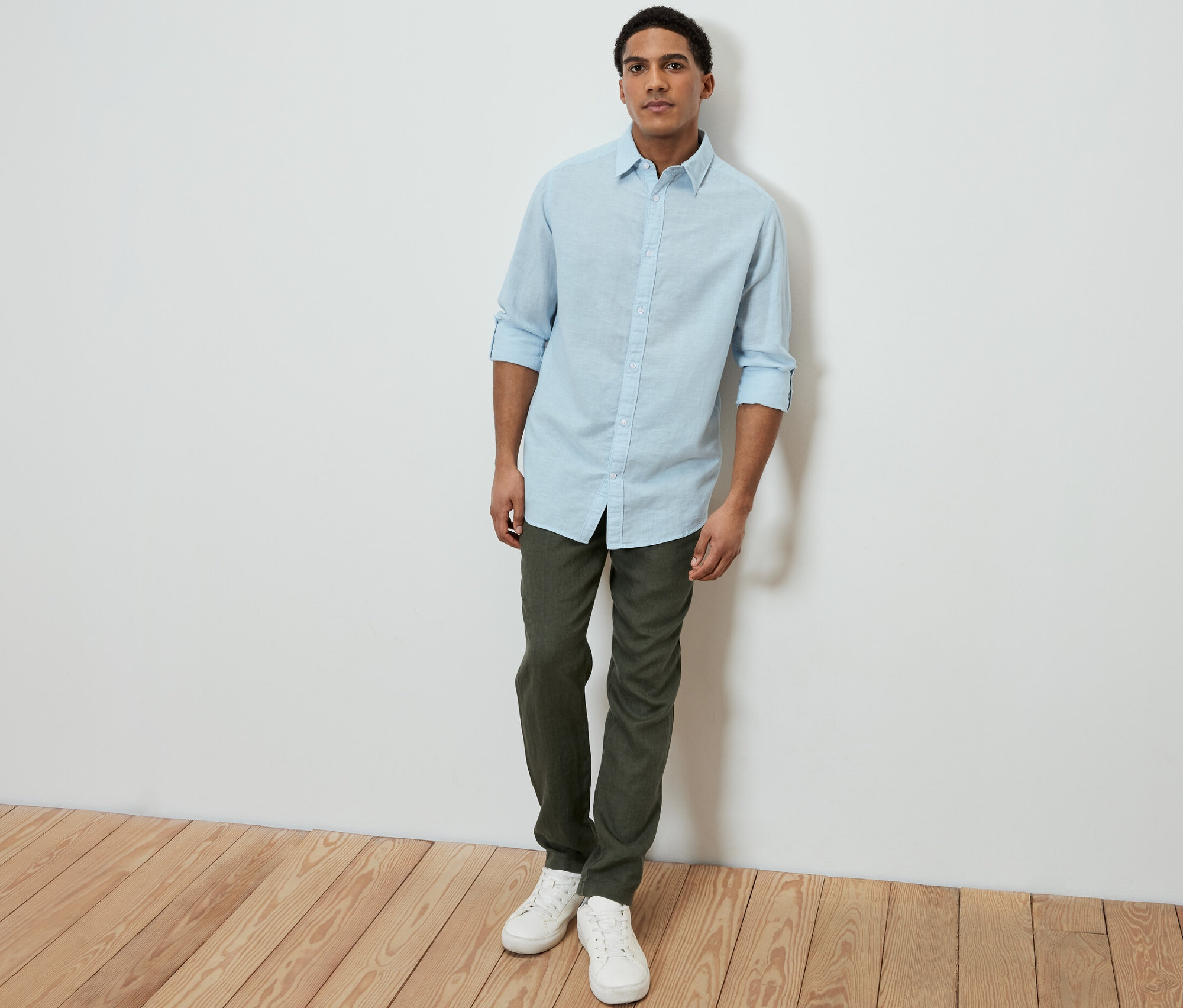 Férfi világoskék lenvászon inget, zöld nadrágot és fehér tornacipőt visel.