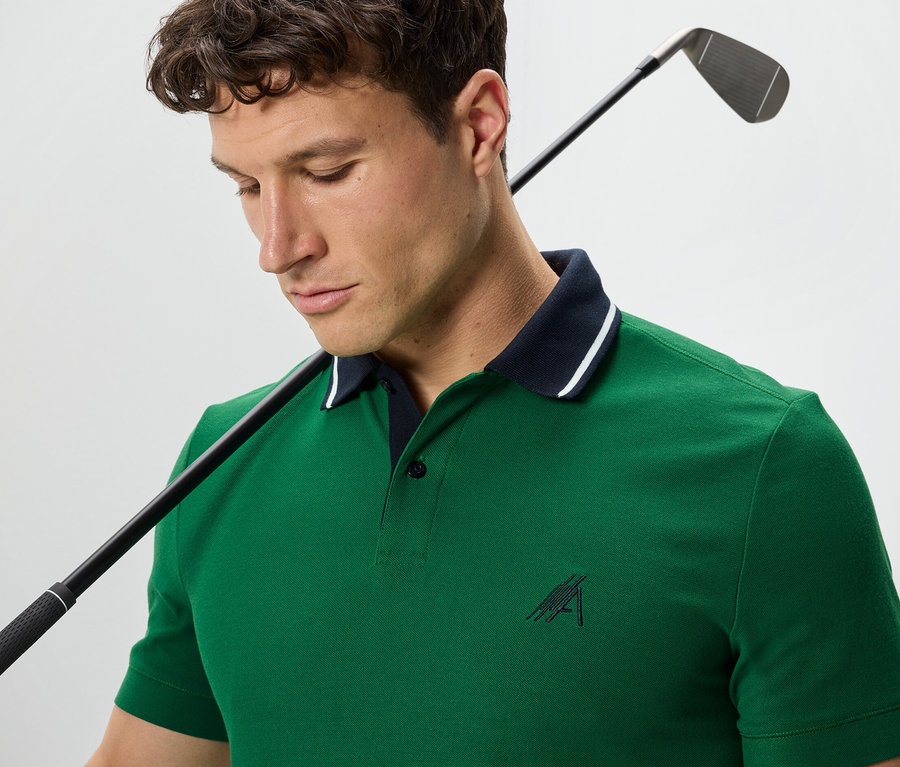 Egy férfi golfütővel a vállán zöld funkcionális pólót visel.