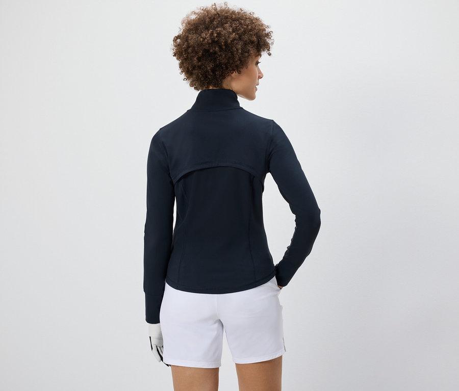 Nő visel funkcionális kabátot és fehér rövidnadrágot.