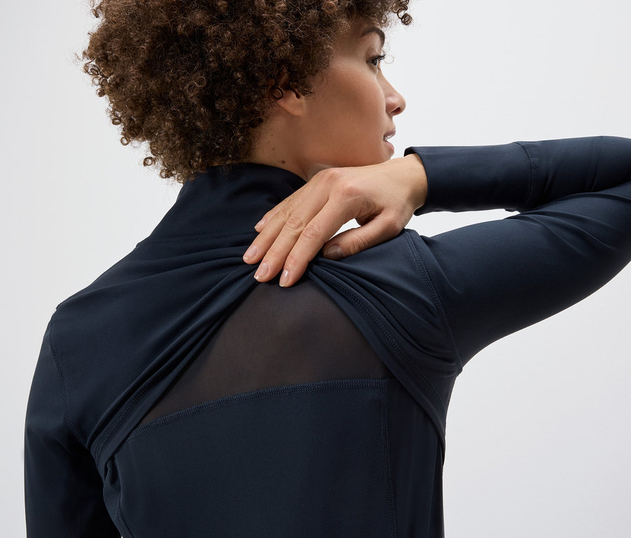 Nő húzza a Férfi funkcionális, kapucnis felső, krém/sötétkék színű felsőt a vállán, hálós betétet mutatva a hátán.