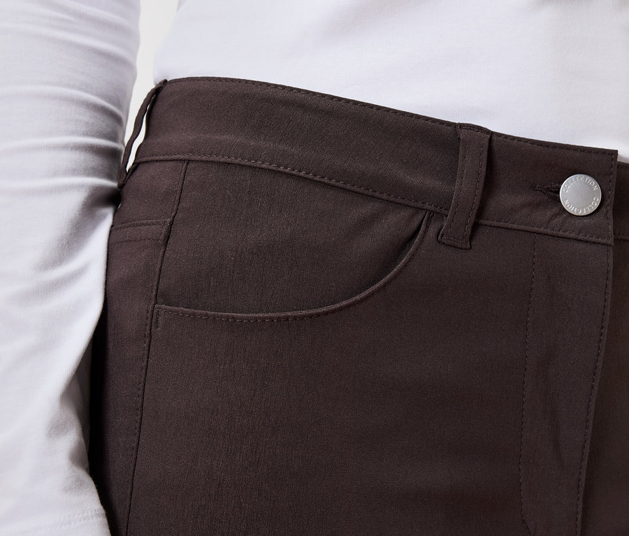 Közeli kép egy hosszú ujjú felsőt és gombos barna nadrágot viselő nőről.