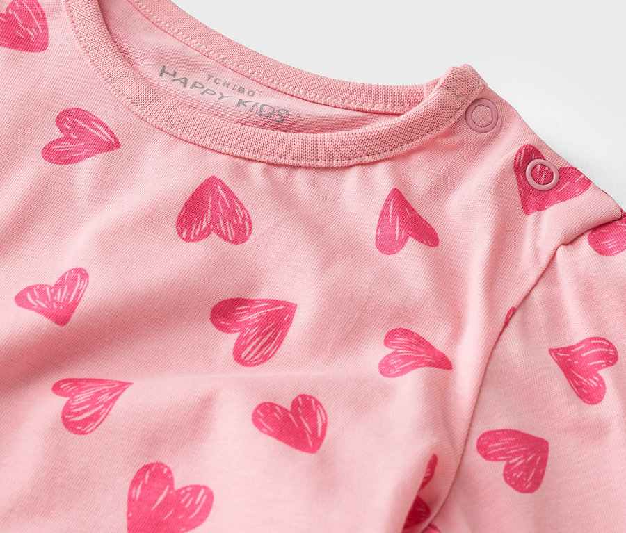 Egy rózsaszín, hosszú ujjú, szívecskés mintázatú póló közeli képe, patentos nyakkal.