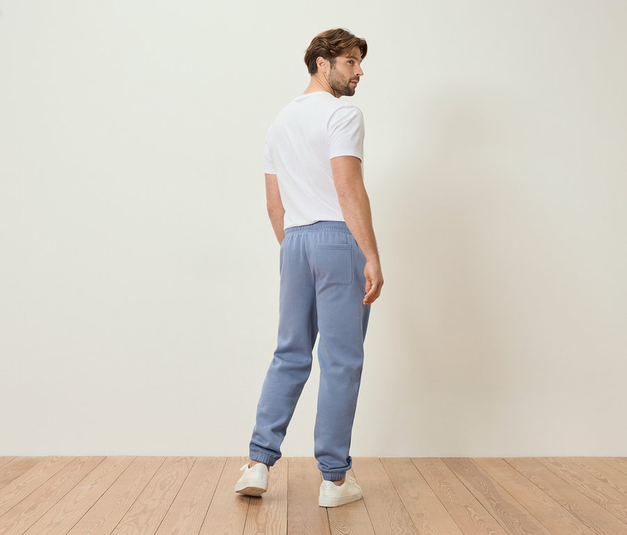 Férfi világoskék joggingalsóban és fehér pólóban, hátulról nézve.