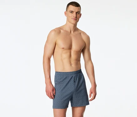 Egy félmeztelen férfi kék, rombuszmintás SCHIESSER jersey boxeralsót visel.