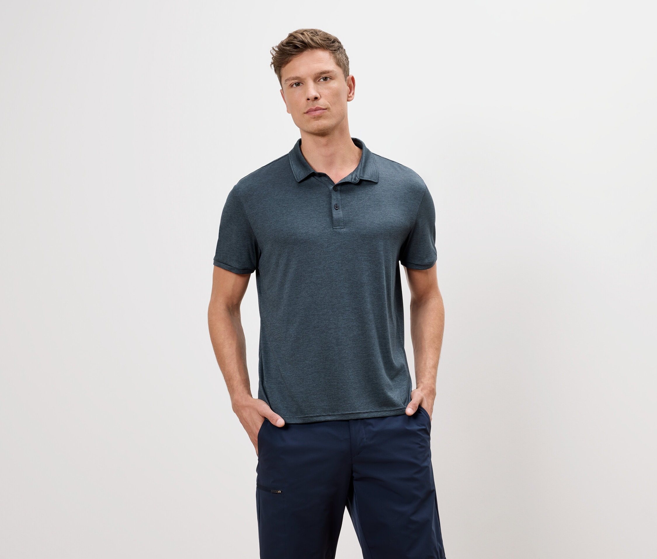 Férfi kék pólóban és kék rövidnadrágban áll fehér háttér előtt.