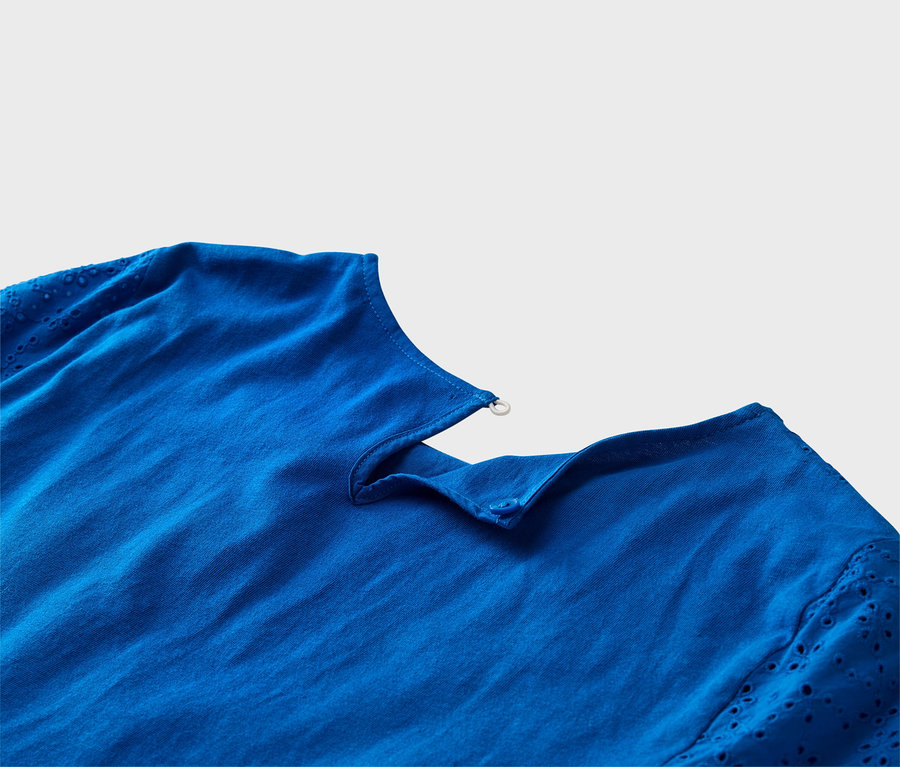 Közeli kép egy kobaltkék felsőről hímzett ujjakkal és gombdíszekkel.