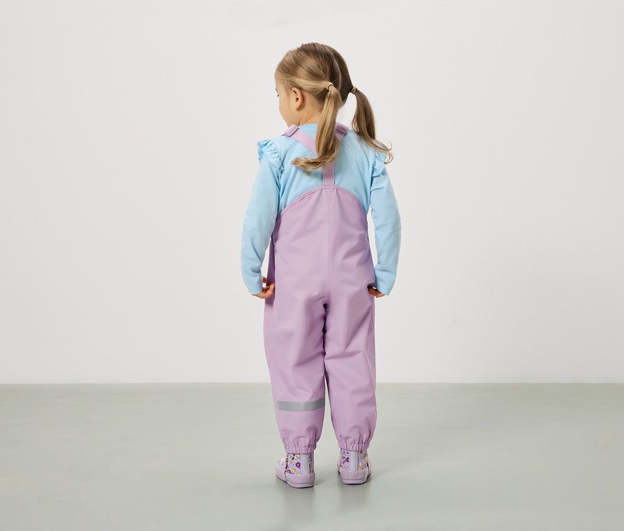 Egy copfos kislány áll háttal a kamerának, lila nadrágot és hozzáillő csizmát visel.