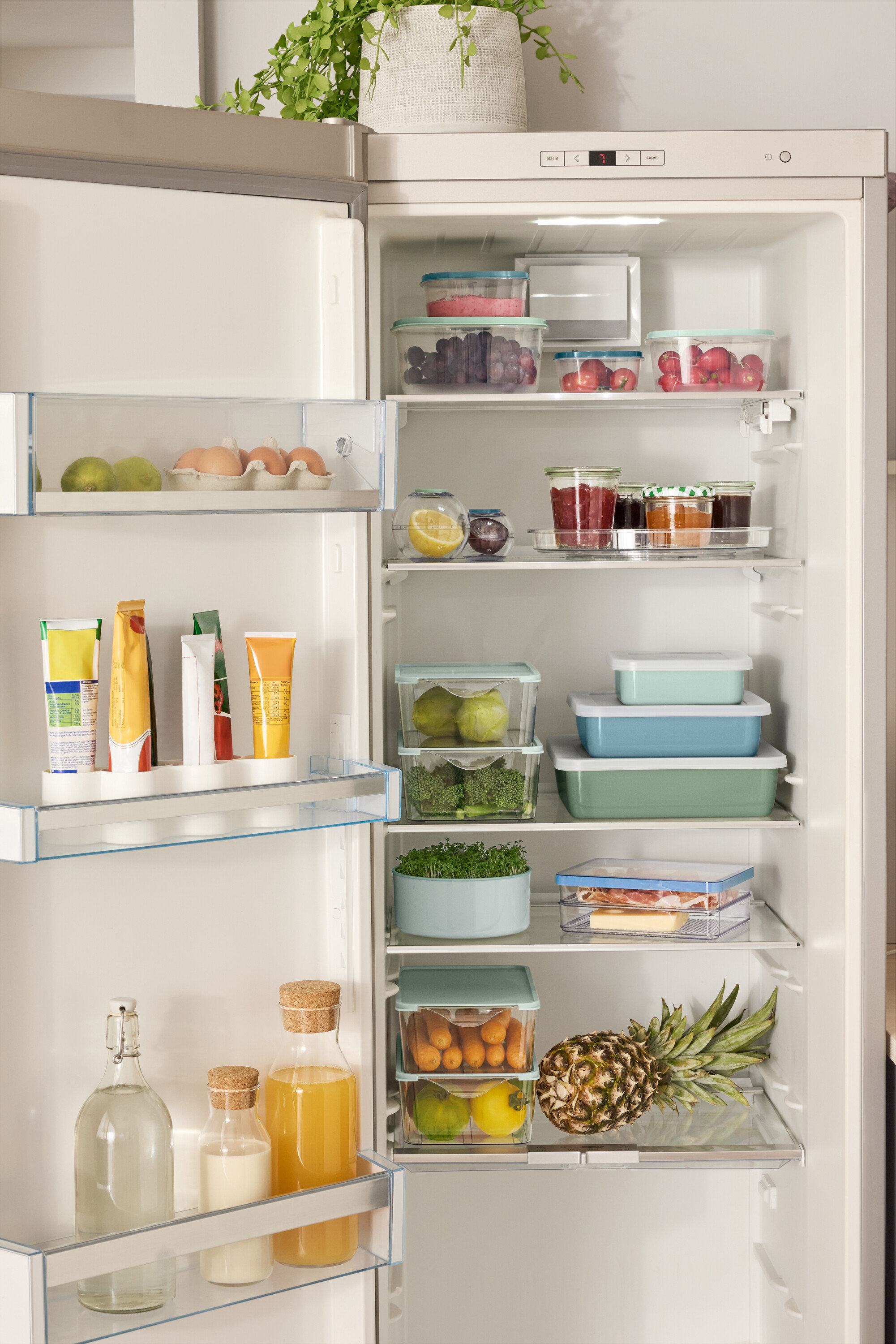 Nyitott hűtőszekrény különféle élelmiszerekkel, köztük 4 db frissentartó doboz készlettel, 2 db frissentartó gömbbel, 3 zománcozott sütőformával fedéllel és egy forgótálcával.